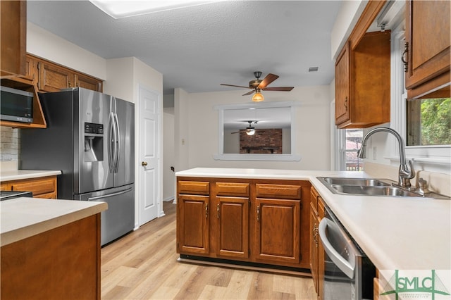 kitchen with light hardwood / wood-style flooring, stainless steel appliances, sink, ceiling fan, and a textured ceiling