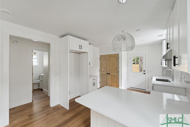 kitchen featuring dark hardwood / wood-style floors, hanging light fixtures, kitchen peninsula, sink, and white cabinetry