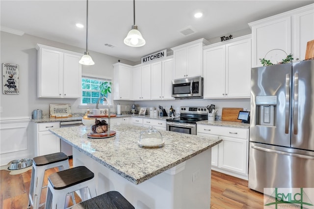 kitchen featuring a center island, decorative light fixtures, appliances with stainless steel finishes, light stone countertops, and white cabinetry