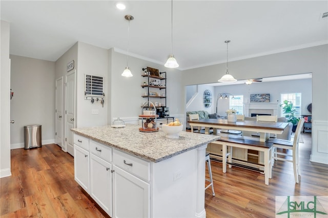 kitchen with a kitchen island, light stone countertops, pendant lighting, wood-type flooring, and white cabinetry