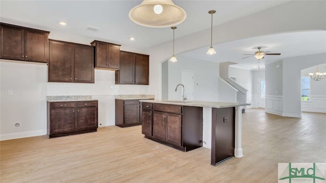 kitchen with ceiling fan with notable chandelier, decorative light fixtures, dark brown cabinets, a center island with sink, and sink