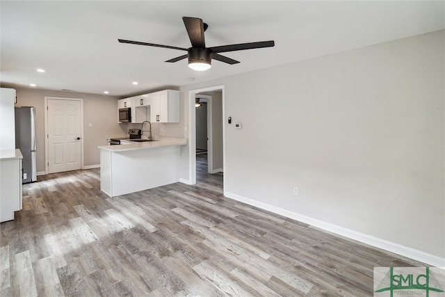 kitchen with stainless steel appliances, kitchen peninsula, ceiling fan, white cabinets, and light hardwood / wood-style floors