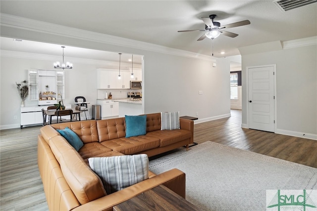 living room with light wood-type flooring, ceiling fan with notable chandelier, and crown molding