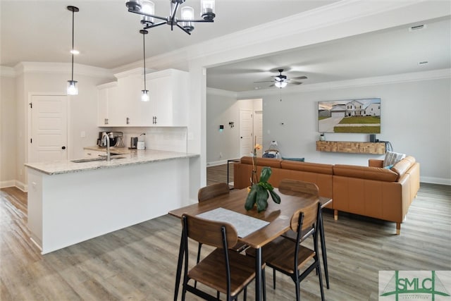 dining area featuring wood-type flooring, ornamental molding, ceiling fan with notable chandelier, and sink