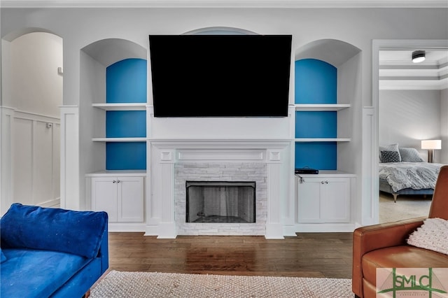 living room featuring dark wood-type flooring, built in features, and a stone fireplace