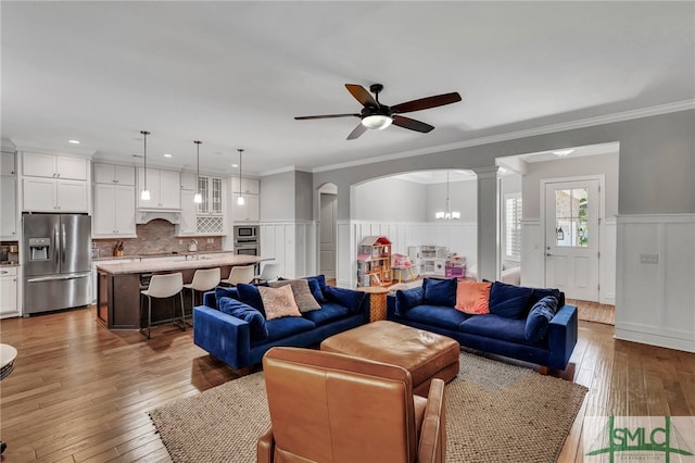 living room featuring ornamental molding, hardwood / wood-style floors, decorative columns, and ceiling fan with notable chandelier