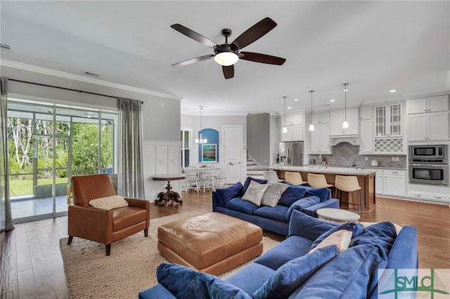 living room featuring light wood-type flooring, ornamental molding, and ceiling fan