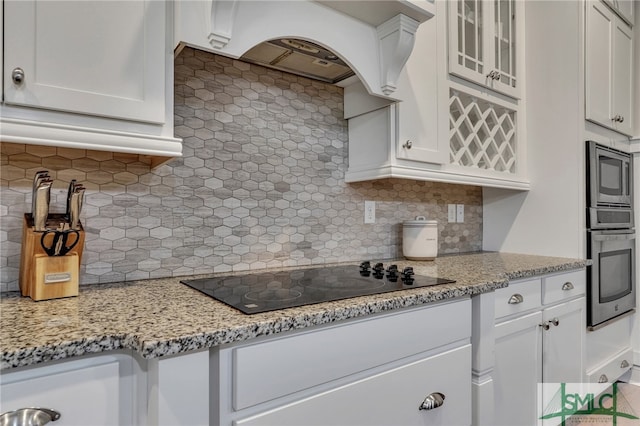 kitchen featuring backsplash, appliances with stainless steel finishes, light stone counters, custom exhaust hood, and white cabinetry