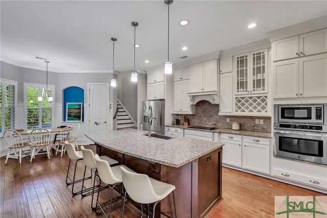 kitchen with appliances with stainless steel finishes, light hardwood / wood-style floors, pendant lighting, a kitchen bar, and a kitchen island with sink