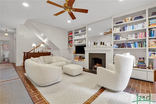 living room featuring ceiling fan, a fireplace, and built in features