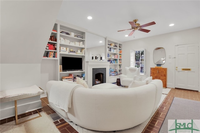 living room featuring ceiling fan, a fireplace, and built in shelves