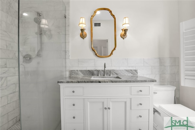 bathroom featuring a tile shower, vanity, toilet, and tile walls