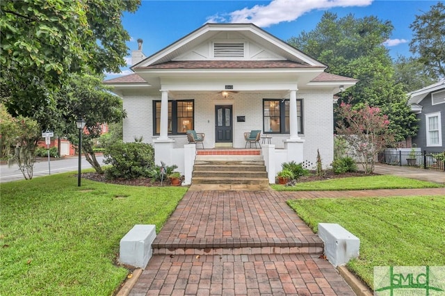 view of front of home with a front yard, fence, brick siding, and covered porch