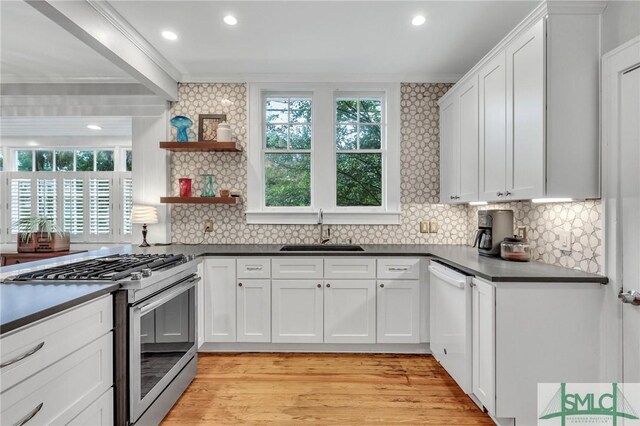 kitchen with light hardwood / wood-style flooring, high end stove, white dishwasher, sink, and white cabinets