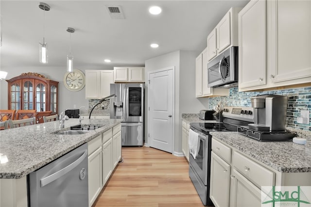 kitchen featuring a kitchen island with sink, white cabinets, hanging light fixtures, light hardwood / wood-style floors, and stainless steel appliances