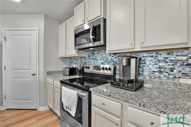 kitchen with light stone countertops, appliances with stainless steel finishes, light wood-type flooring, backsplash, and white cabinets