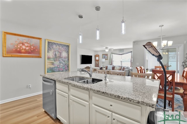 kitchen featuring stainless steel dishwasher, sink, pendant lighting, white cabinets, and an island with sink