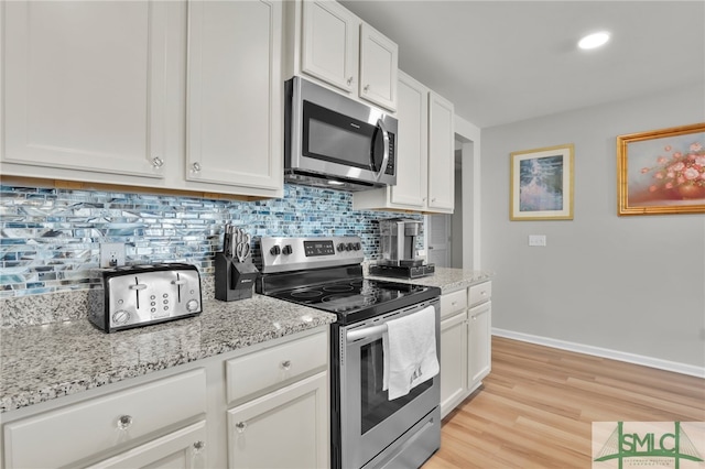 kitchen with decorative backsplash, stainless steel appliances, white cabinetry, and light stone countertops