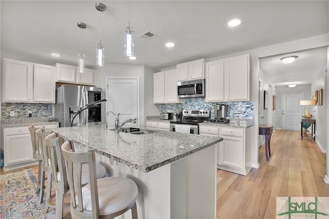 kitchen featuring white cabinetry, sink, stainless steel appliances, light hardwood / wood-style flooring, and pendant lighting