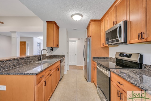 kitchen featuring a textured ceiling, light tile patterned floors, appliances with stainless steel finishes, sink, and dark stone counters