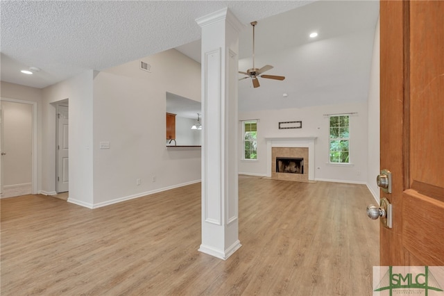 unfurnished living room featuring a tiled fireplace, light wood-type flooring, a textured ceiling, and ceiling fan