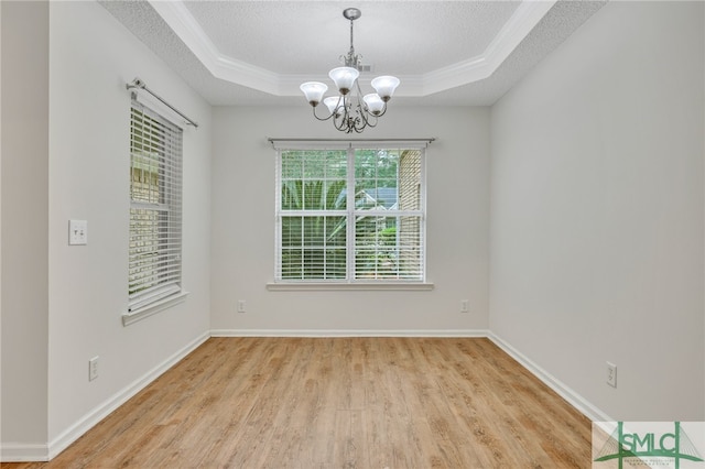 empty room with a tray ceiling, light wood-type flooring, and an inviting chandelier