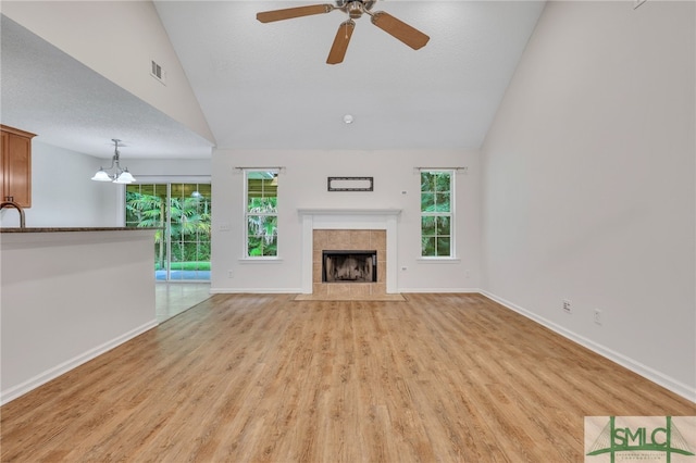 unfurnished living room with a fireplace, light hardwood / wood-style flooring, ceiling fan with notable chandelier, lofted ceiling, and a textured ceiling