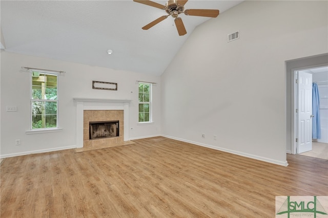 unfurnished living room with high vaulted ceiling, ceiling fan, a tiled fireplace, and light wood-type flooring