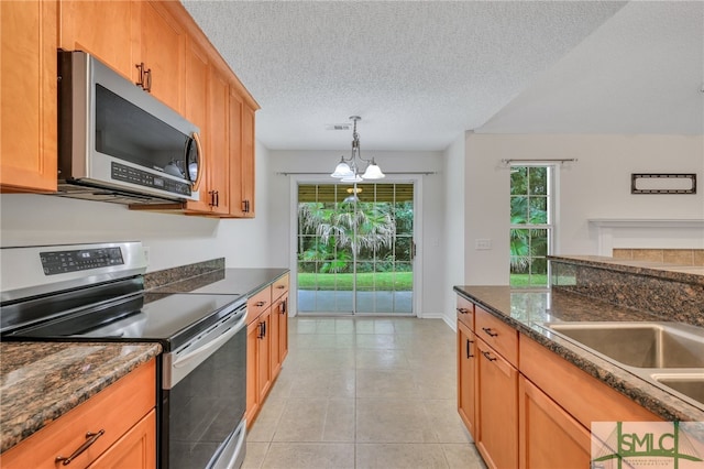 kitchen with a textured ceiling, pendant lighting, a notable chandelier, appliances with stainless steel finishes, and dark stone counters