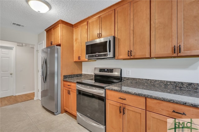 kitchen with a textured ceiling, dark stone countertops, light tile patterned floors, and appliances with stainless steel finishes