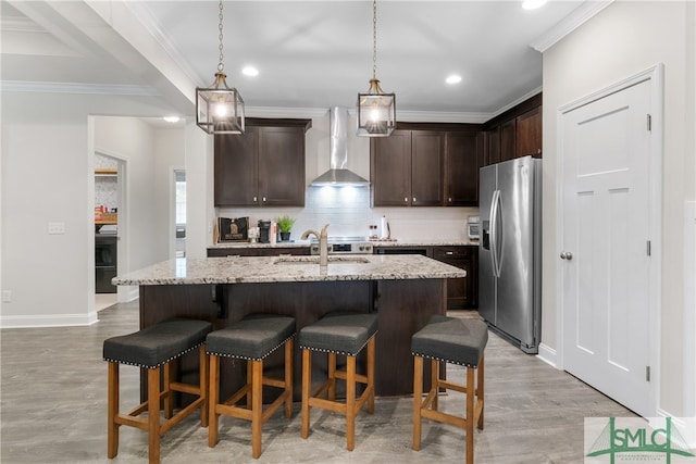 kitchen featuring light stone counters, light hardwood / wood-style floors, wall chimney range hood, an island with sink, and stainless steel fridge with ice dispenser