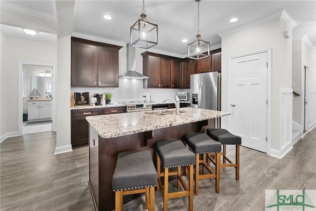 kitchen with hanging light fixtures, hardwood / wood-style floors, wall chimney range hood, a kitchen breakfast bar, and a center island with sink