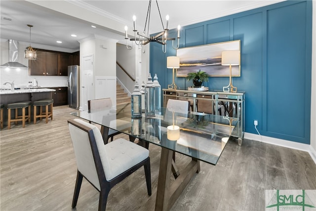 dining room with light hardwood / wood-style flooring, sink, a notable chandelier, and ornamental molding