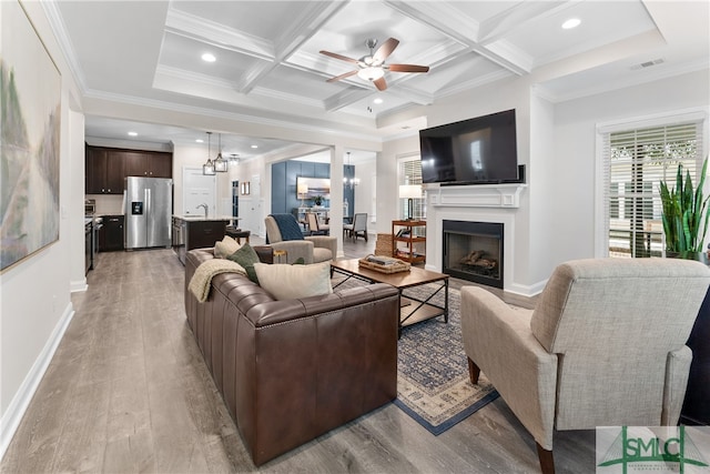 living room featuring coffered ceiling, ceiling fan with notable chandelier, light wood-type flooring, and beam ceiling