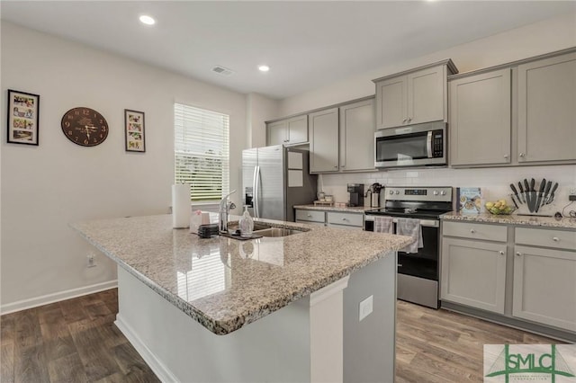 kitchen with a center island with sink, dark wood finished floors, a sink, gray cabinetry, and appliances with stainless steel finishes