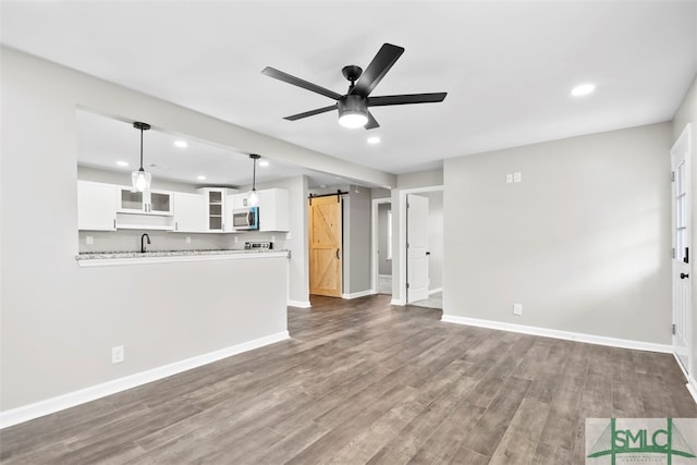 unfurnished living room with wood-type flooring, sink, ceiling fan, and a barn door