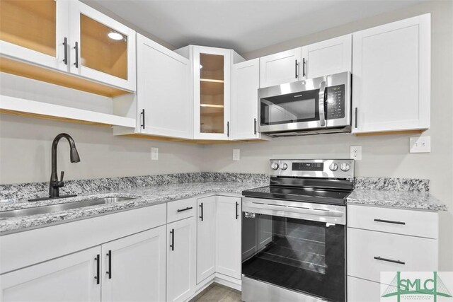 kitchen featuring hardwood / wood-style floors, stainless steel appliances, light stone counters, sink, and white cabinets