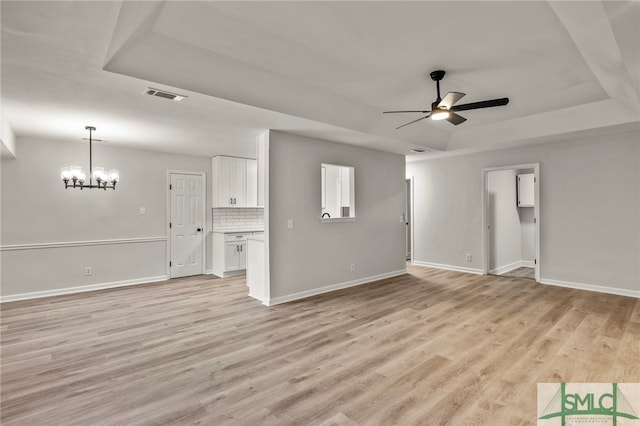 unfurnished living room featuring ceiling fan with notable chandelier, a tray ceiling, and light hardwood / wood-style floors