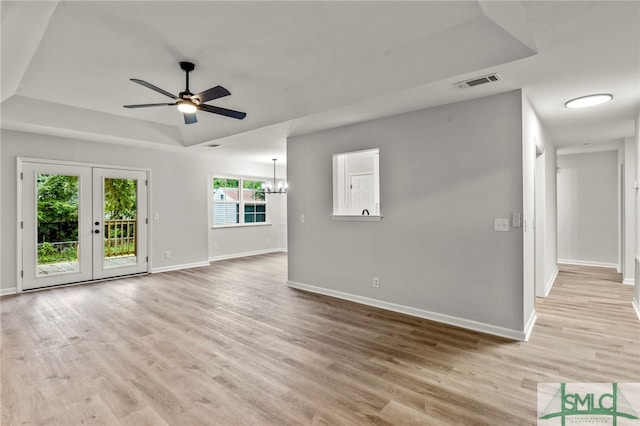 unfurnished living room with ceiling fan with notable chandelier, french doors, a healthy amount of sunlight, and light hardwood / wood-style floors