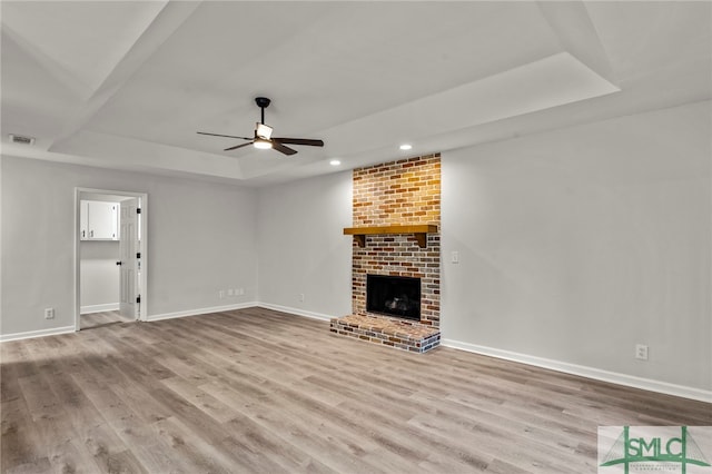 unfurnished living room with a fireplace, a tray ceiling, ceiling fan, and light hardwood / wood-style floors