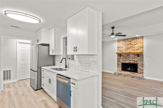 kitchen with light wood-type flooring, stainless steel appliances, white cabinetry, sink, and ceiling fan