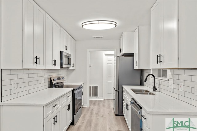 kitchen with light wood-type flooring, sink, appliances with stainless steel finishes, and white cabinets