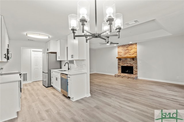 kitchen featuring ceiling fan with notable chandelier, a fireplace, light hardwood / wood-style flooring, stainless steel appliances, and white cabinetry