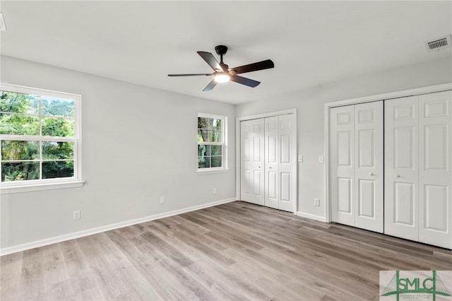 unfurnished bedroom with light hardwood / wood-style flooring, multiple windows, ceiling fan, and two closets