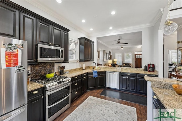 kitchen with appliances with stainless steel finishes, ornamental molding, open floor plan, a healthy amount of sunlight, and light stone countertops