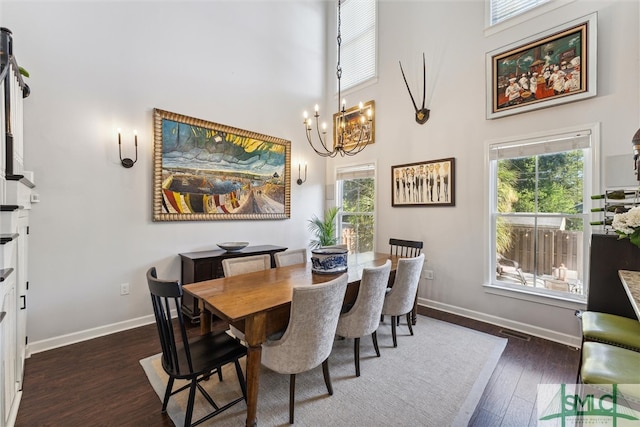 dining space with a towering ceiling, dark wood-type flooring, and a chandelier