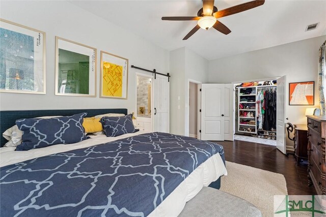 bedroom with a closet, dark hardwood / wood-style floors, a barn door, ensuite bath, and ceiling fan