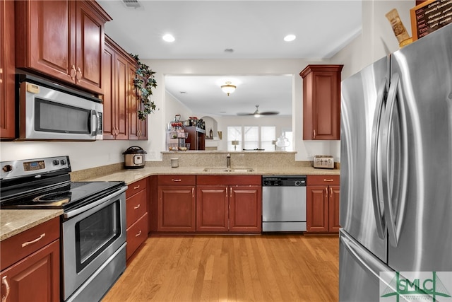 kitchen with light stone counters, stainless steel appliances, sink, and light hardwood / wood-style flooring