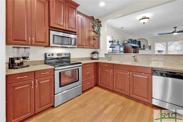 kitchen with stainless steel appliances, light stone counters, sink, ceiling fan, and light hardwood / wood-style floors