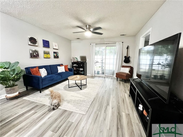 living room featuring light wood-type flooring, a textured ceiling, and ceiling fan